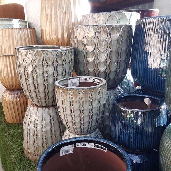 Une collection de pots de plantes en céramique de différentes tailles et motifs. Les pots sont empilés et disposés sur une surface herbeuse, avec des motifs texturés et des couleurs variées, incluant des tons de gris, bleu et brun.